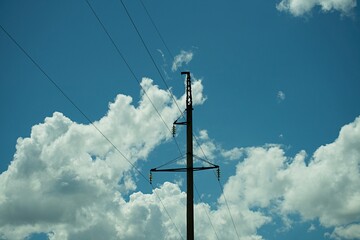 Obraz premium High voltage electric concrete pole and power lines against blue sky with white clouds background