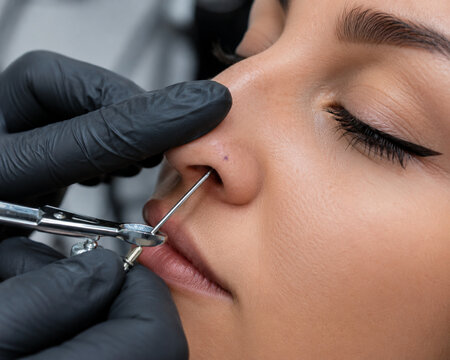 Woman getting nose piercing in beauty studio close up