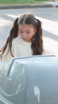 Young Asian Girl with Pigtails Disposing of Trash in Park Bin