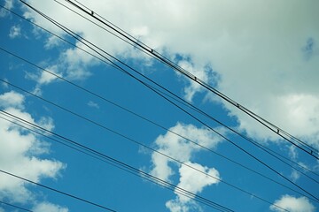 Fototapeta premium Power lines against a beautiful blue sky with white fluffy clouds on a sunny day