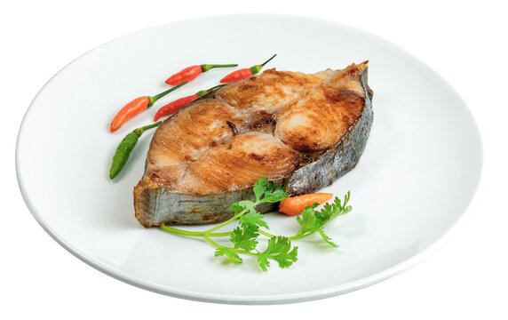 Pan-fried king mackerel fish steak served on a white plate garnished with fresh coriander and bird eye chili peppers. Isolated for food and restaurant concepts.
