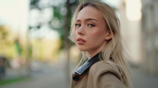 Slow motion portrait of a beautiful young woman with blonde hair turning her head to look at the camera with a seductive gaze while walking on a city street during the daytime