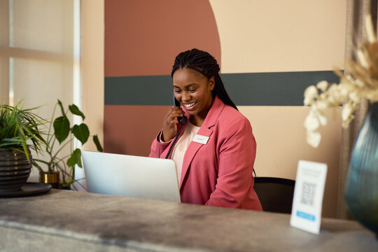 African receptionist working while talking on phone at desk