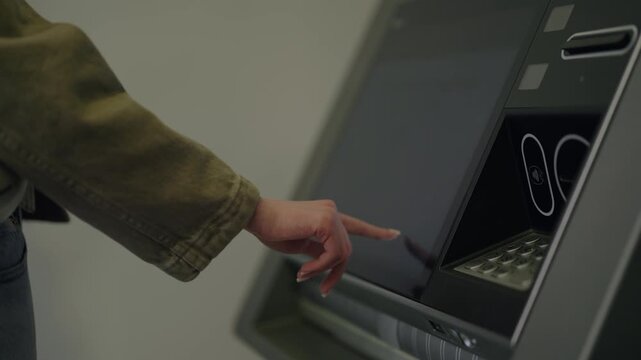 Close-up of a woman's hand using a self-service machine, touching the screen to make a payment or withdraw cash, with the contactless reader lighting up to confirm the transaction