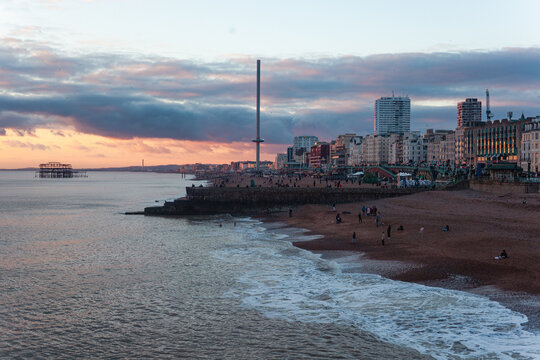 Brighton seafront at sunset with the ruined West Pier and i360 observation tower silhouetted against a dramatic pink and grey sky
