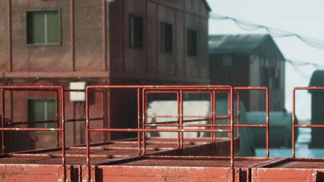 Workers are seen preparing a metal platform near a red building in a busy construction area. The scene shows tools and equipment scattered around, indicating active work.
