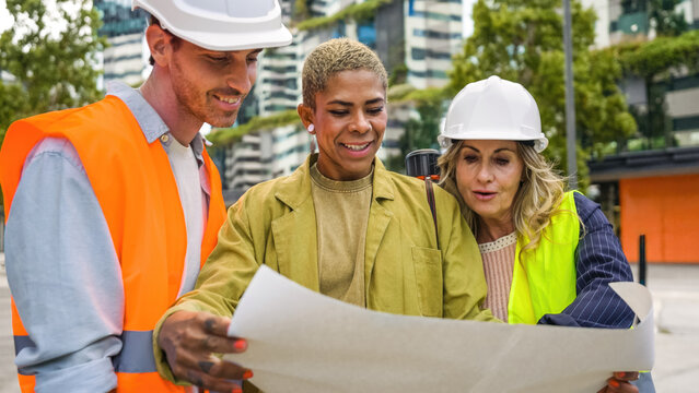 Diverse professional team collaborating on an urban development project, looking at plans and discussing new designs on site