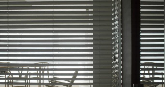 Mysterious backlit silhouette of an anonymous person walking inside a modern corporate office, seen from the outside through the horizontal slats of the window blinds in slow motion