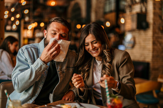 Couple enjoying dinner date, man sneezing, woman laughing at restaurant