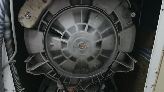 Back view of a washing machine drum pulley spinning during repair. Technical maintenance and diagnostic of domestic appliance.
