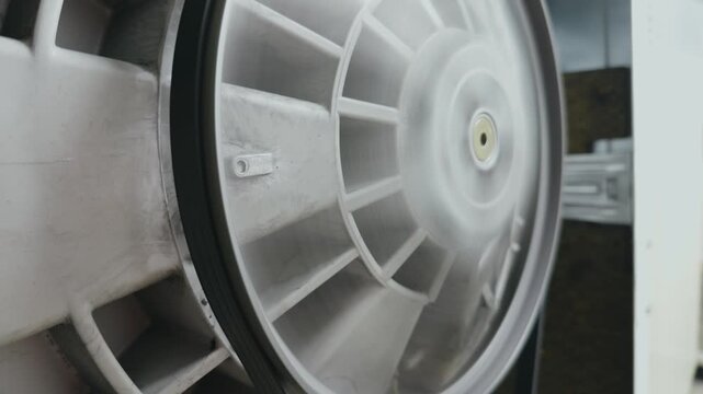 Back view of a washing machine drum pulley spinning during repair. Technical maintenance and diagnostic of domestic appliance.