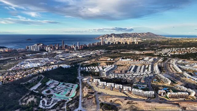 Coastal housing development at sunrise with sprawling suburbs, winding roads, turquoise pools and distant