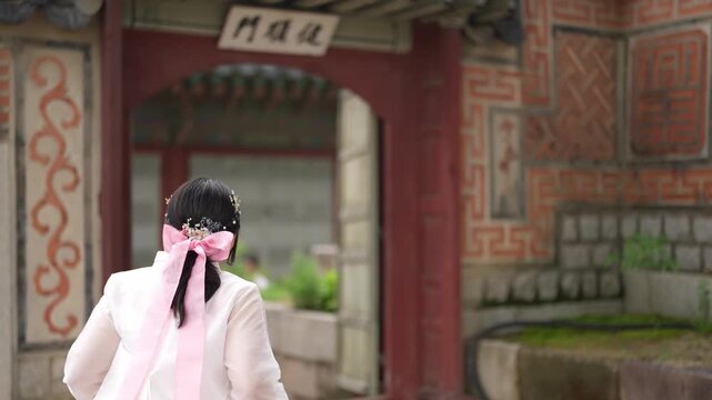 Two young girls walk through a traditional gate. They wear flowing hanboks with matching ribbons. Soft light bathes their delicate silhouettes. Their steps echo gently on ancient stone