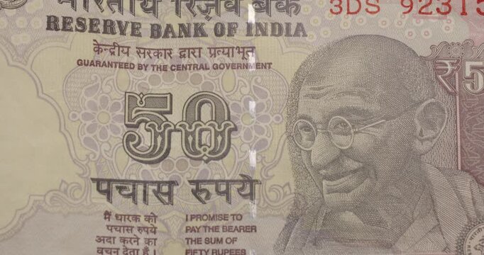 Macro view of a fifty Indian rupee banknote sliding downwards, detailing the portrait of Mahatma Gandhi, the security features, and the intricate design of the official currency of India