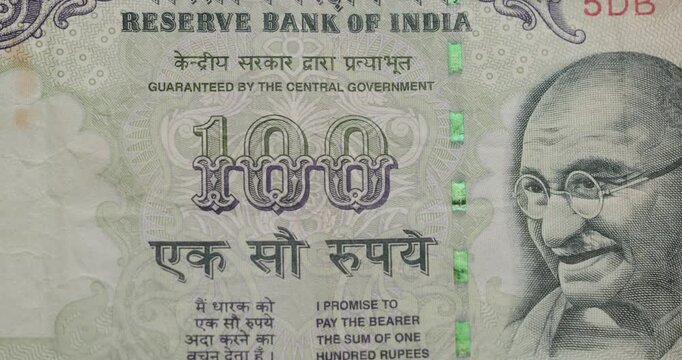 Extreme close-up of a one hundred Indian rupee banknote, focusing on the portrait of Mahatma Gandhi and the security thread, representing India's economic growth and financial system
