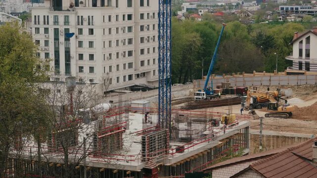 Busy construction site timelapse showing workers and machinery building the foundation of a modern residential building in an urban area, with heavy equipment like cranes and excavators at work