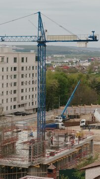 Dynamic timelapse capturing a tower crane in operation as builders work on a new concrete building, with trucks and equipment moving around the urban construction site during a cloudy day