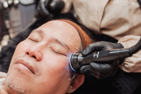 Professional esthetician performing a Hydra Oxygen Facial with a facial ultrasound sonophoresis probe on crow's feet area of a middle-aged man to enhance serum absorption and skin hydration.