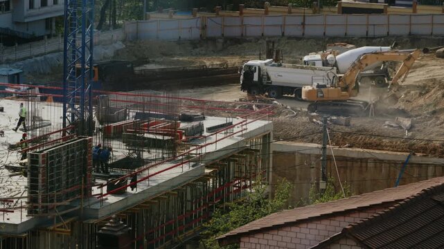 Construction workers building a reinforced concrete structure while an excavator moves earth and a concrete mixer truck works nearby, showing the initial stages of a large building project. timelapse