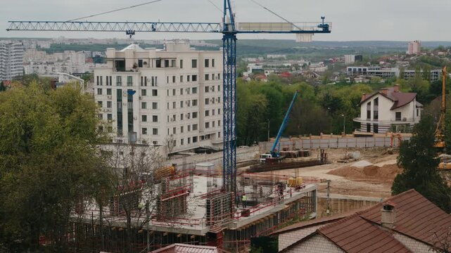 Urban construction site in a city showing a tower crane operating and workers building the foundation and structure of a new residential block. Capturing the rapid development and real estate growth