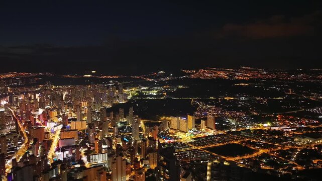 Night aerial city skyline glowing with neon lights and busy streets, sweeping drone reveal of beachfront