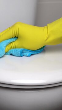 Hand in a yellow rubber glove with blue rag cleaning the toilet in the bathroom. Disinfect and sanitary standards.Scrubbing and cleaning.