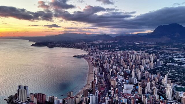 Dusk city skyline with bay, aerial sweep over dense highrise district, lively coastline, pastel sunset