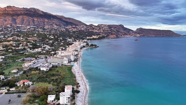 Aerial sunrise coastal town with bay and calm turquoise waters, sandy shoreline and mountain backdrop morning