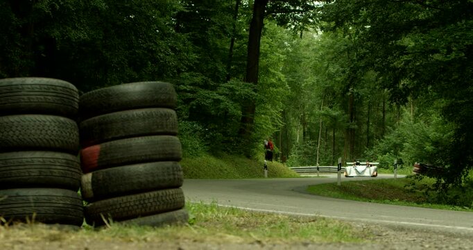 White and orange race car driving on a curved asphalt road through a green forest