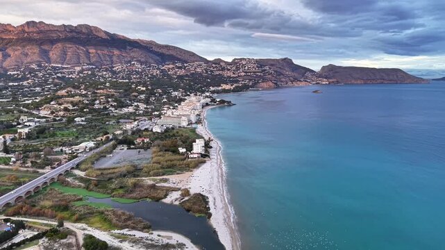 Aerial beach bay with turquoise water and shoreline resort, promotion shot highlights villas, promenade, palms