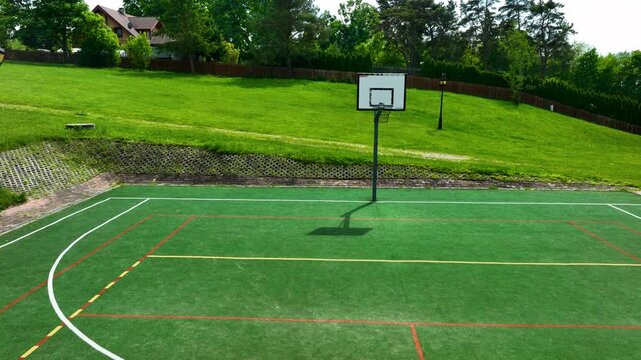 An empty green multisport court featuring a basketball hoop and volleyball net, located in the scenic Masuria region of Poland. Perfect for sports, wellness, and recreation themes.