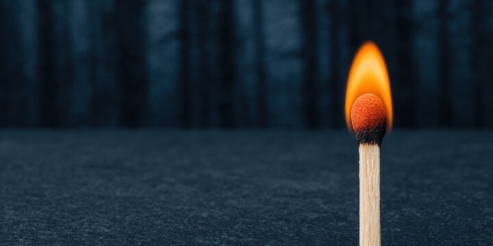 Burning matchstick with bright orange flame isolated on dark background representing fire ignition and energy concept for creative photography projects