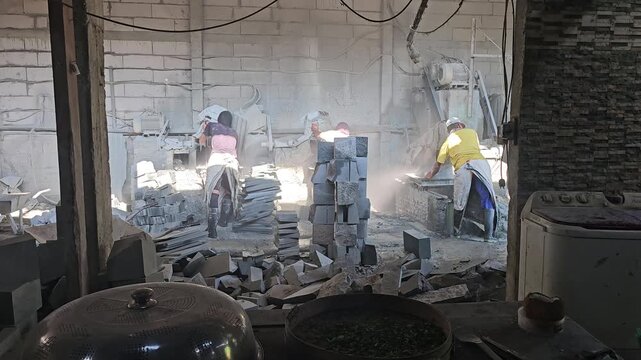Workers in a dusty workshop cutting stone blocks into tiles using electric circular saws