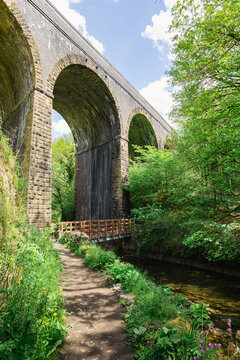 Footpath leading beneath a Victorian stone railway viaduct beside a stream in a lush green wooded valley in spring