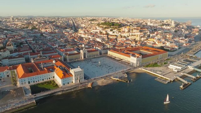 Slow panoramic drone pan of Praca do Comercio, Lisbon at sunset. Square in shadow, warm golden sky beyond. Clear cloudless sky. Portugal