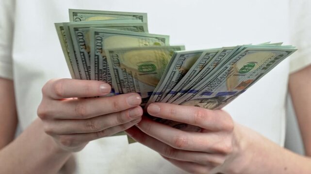Woman in white t-shirt counting stack of dollar banknotes. Personal finance, cash savings, income, wealth, investment, budgeting and money management concept.	
