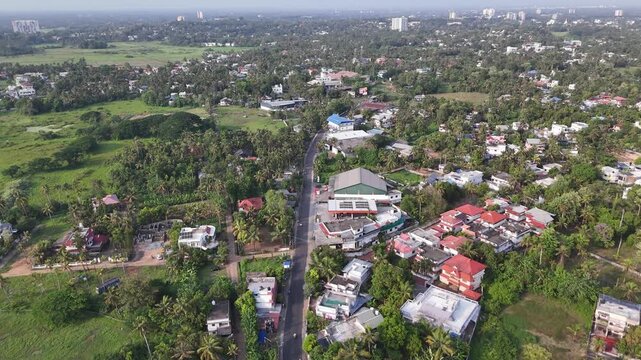 Aluva with colorful homes, tree-covered communities, agricultural fields, and winding local roads extending toward the distant skyline of the Kochi metropolitan region.