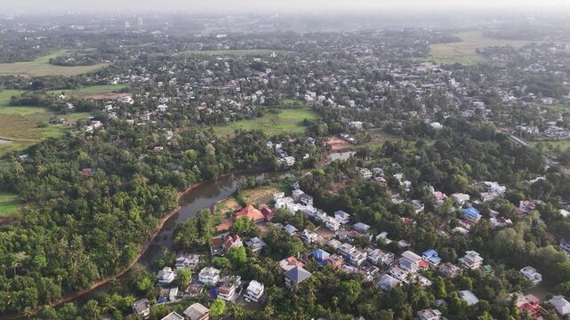 Aluva with colorful homes, tree-covered communities, agricultural fields, and winding local roads extending toward the distant skyline of the Kochi metropolitan region.