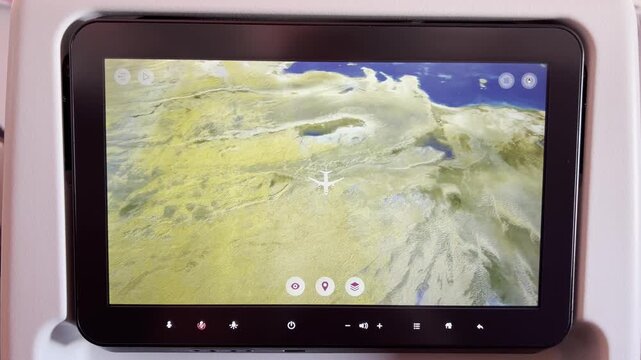 A close-up view of an airplane seat-back entertainment screen displaying a 3D flight tracking map over a desert region with a body of water in the distance.