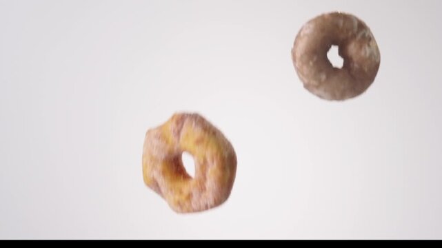 Assorted glazed and chocolate donuts raining down on white seamless backdrop in cinematic slow motion. donut shop branding, coffee chain ads, office breakfast catering posts.