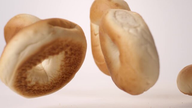 Pile of chewy golden bagels tumbling and bouncing on bright white backdrop in slow motion. office breakfast reels, weekend brunch videos, jewish bakery content.