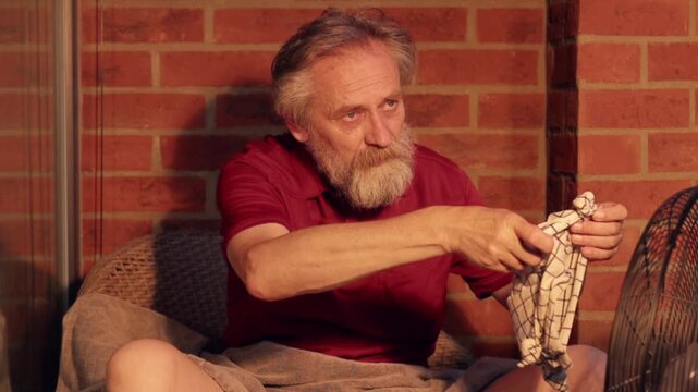 Elderly man struggling with extreme summer heatwave on his city apartment balcony