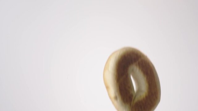 Chewy golden bagels raining down on white seamless backdrop in cinematic slow motion. new york deli content, bagel shop branding, brunch menu reels.
