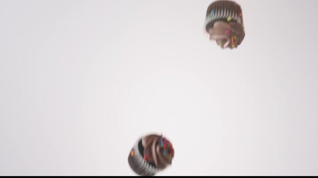 Pastel frosted bite-size cupcakes raining down on white seamless backdrop in cinematic slow motion. baby shower content, kids birthday party reels, gender reveal videos.