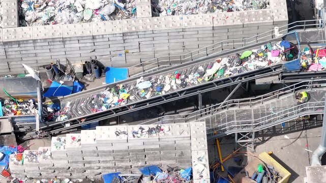 A waste recycling facility processes plastic waste. Workers sort materials on conveyor belts. Equipment moves recyclable items for further processing. Facility operates for waste management.