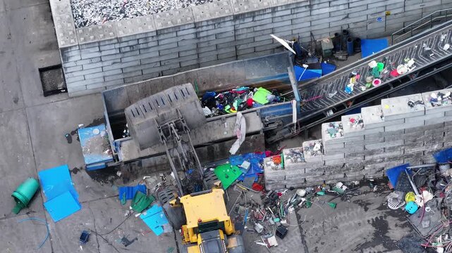 Plastic waste enters the facility on a conveyor belt. Workers sort recyclable materials from non-recyclable. Machinery processes plastic for recovery.