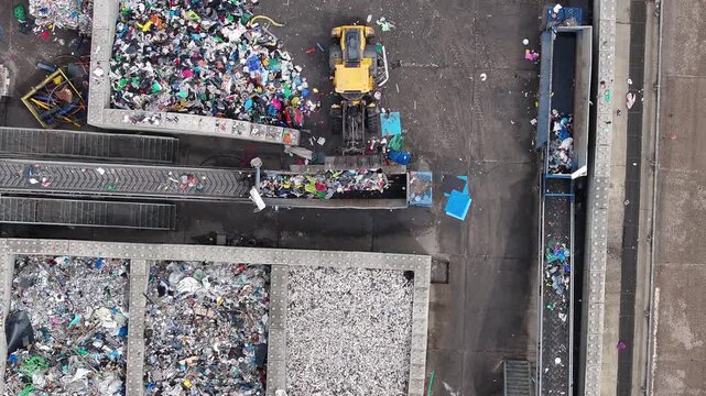 Plastic waste is sorted and processed in a recycling facility. Heavy machinery moves materials for recovery. Various types of plastic waste are collected for processing.