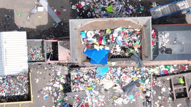 Plastic waste enters the processing area of a recycling facility. Conveyor belts transport materials for sorting and recovery. Workers manage recyclable materials for waste reduction.