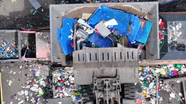 Large machinery loads plastic waste into a processing area for sorting and recovery. Recyclable materials are separated for further processing. The facility operates to support waste management.