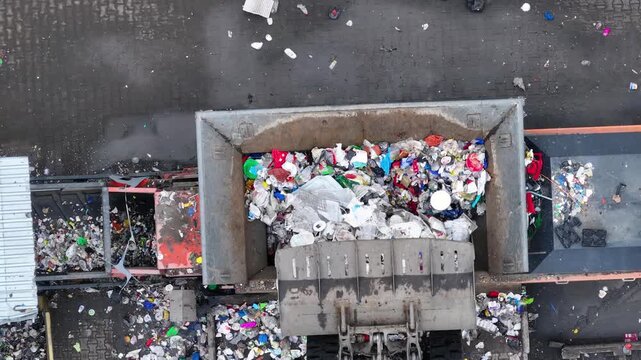 Waste containers are unloading plastic waste at the recycling plant. Machines sort and process various materials. Operations focus on waste management and resource recovery initiatives.